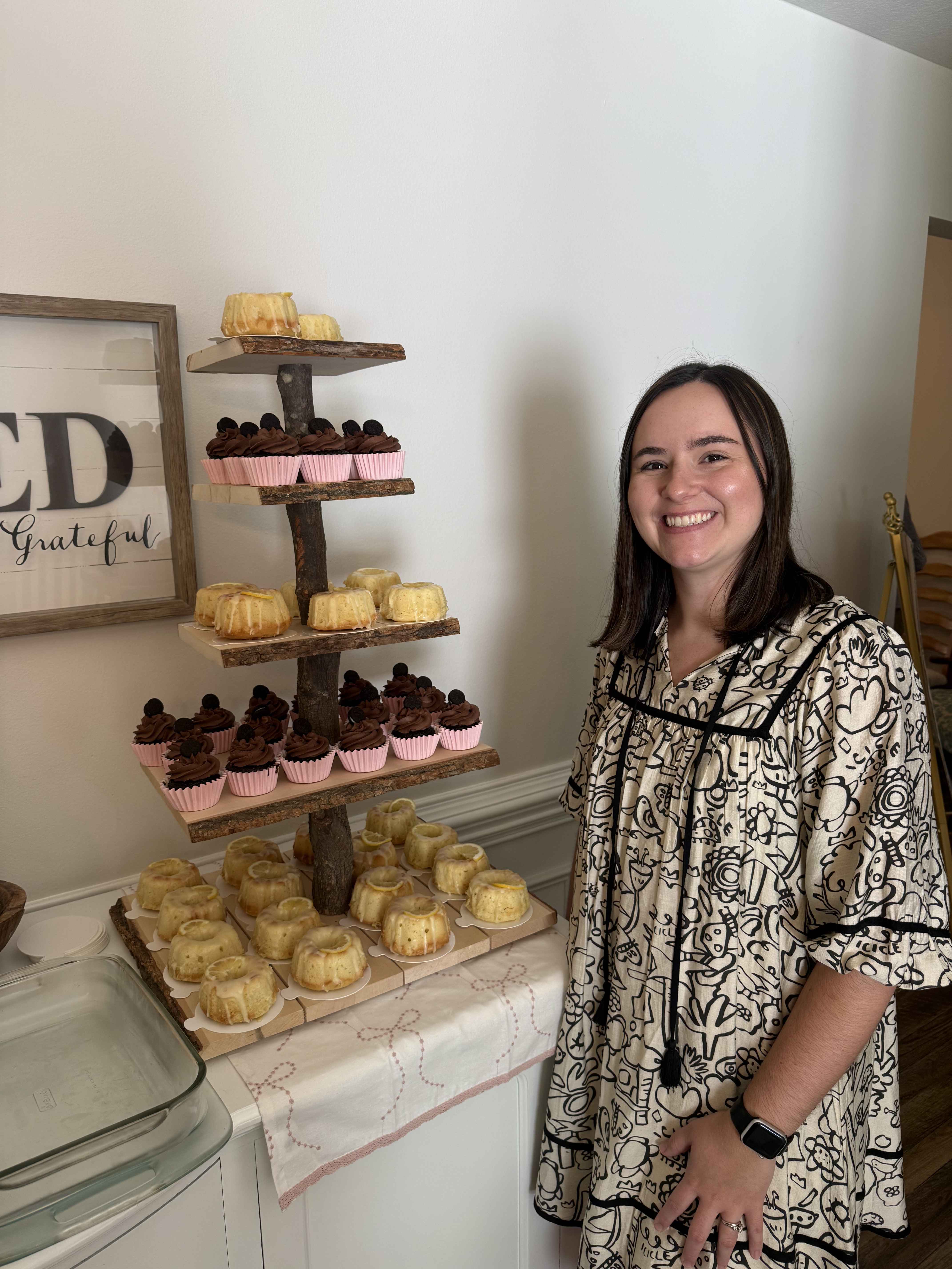 Casie beside a tiered dessert stand with bundt cakes and chocolate cupcakes
